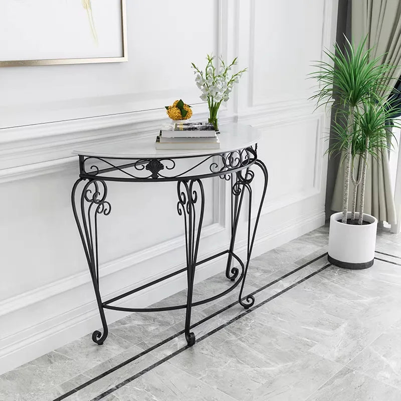 A black wrought-iron console table with a white marble top, styled in a bright, modern room with a potted plant and books on the tabletop.