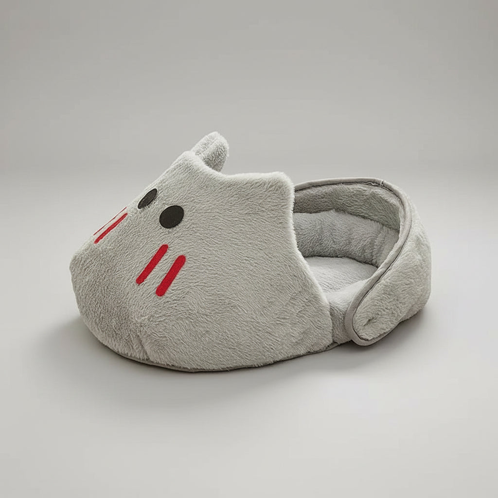 A plush gray cat-shaped pet bed with embroidered red whiskers, black eyes, and small ears, placed on a geometric patterned rug in a room setting.