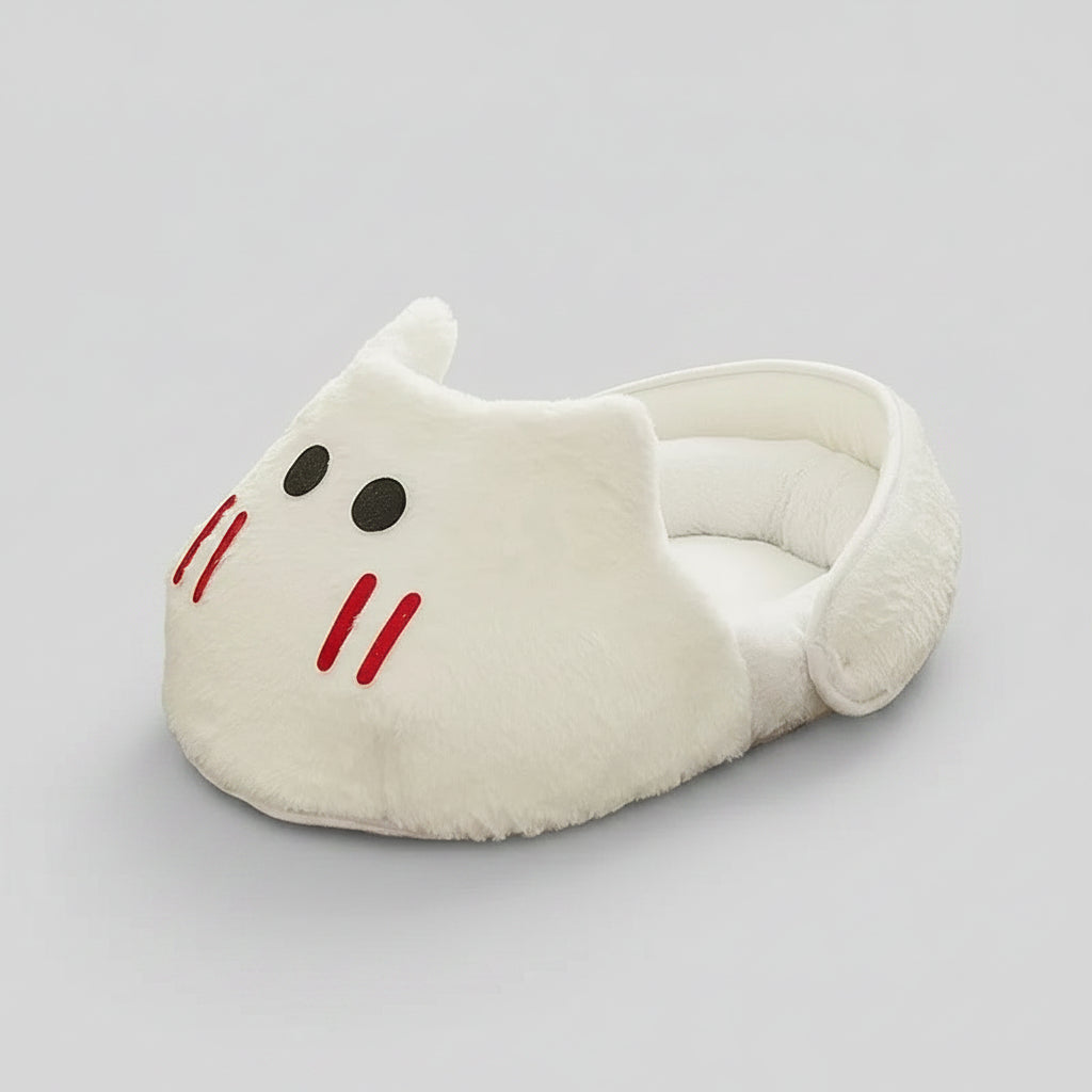A plush white cat-shaped slipper or small pet bed with embroidered black eyes and red whiskers, placed on a geometric patterned rug in a room setting.