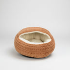 A round, waffle-textured pet bed in a warm tan-brown color with a soft cream-colored fleece lining, shown on a solid white background.