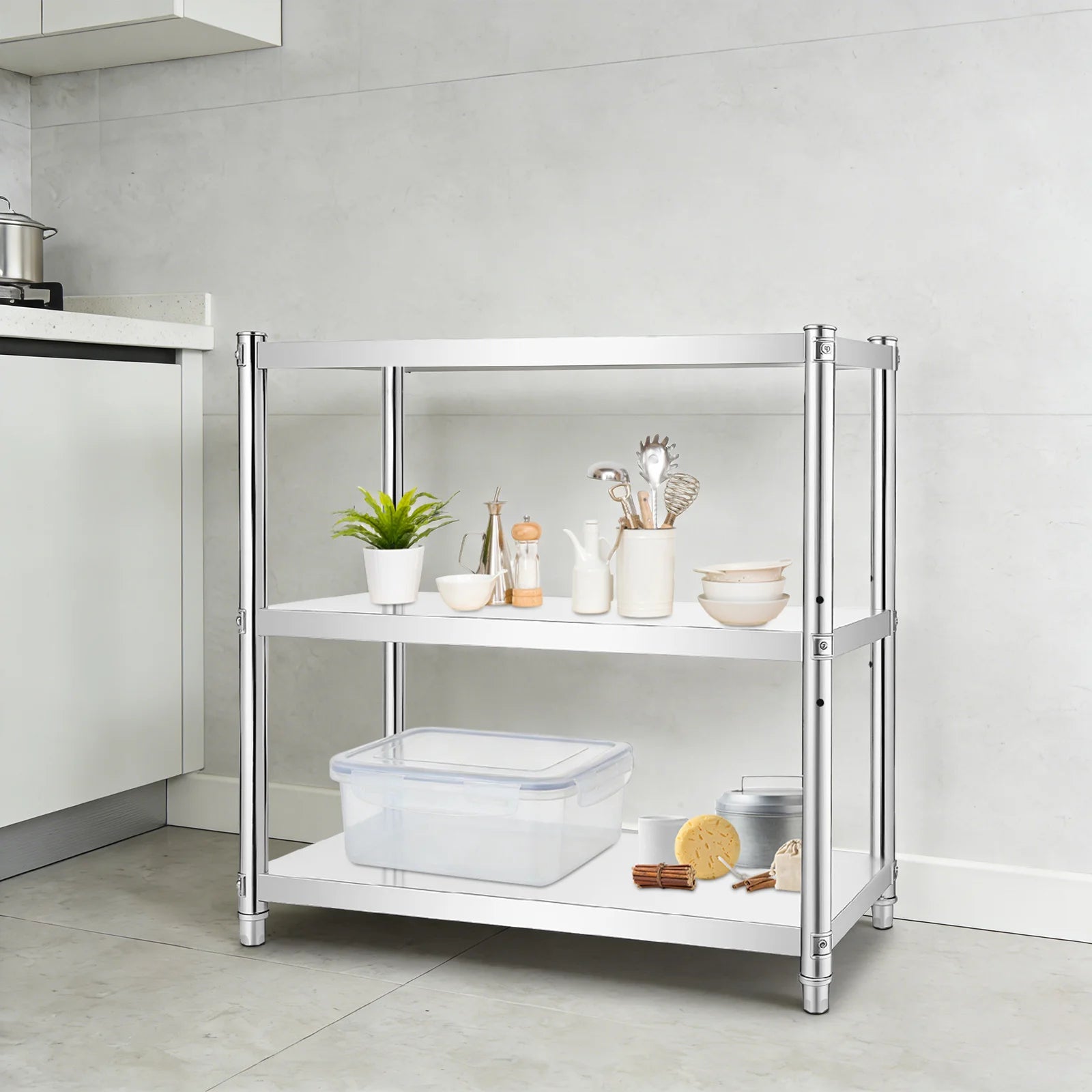 A three-tier kitchen organizer shelf with a chrome silver metal frame and white shelves, styled with kitchenware and food items in a modern kitchen setting.