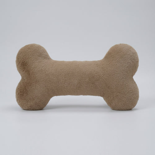 Beige bone-shaped pillow on a textured surface with a magazine underneath