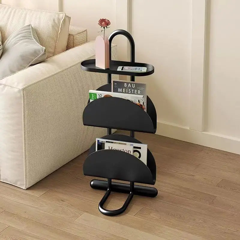 Black magazine rack with books on a wooden floor next to a beige sofa.