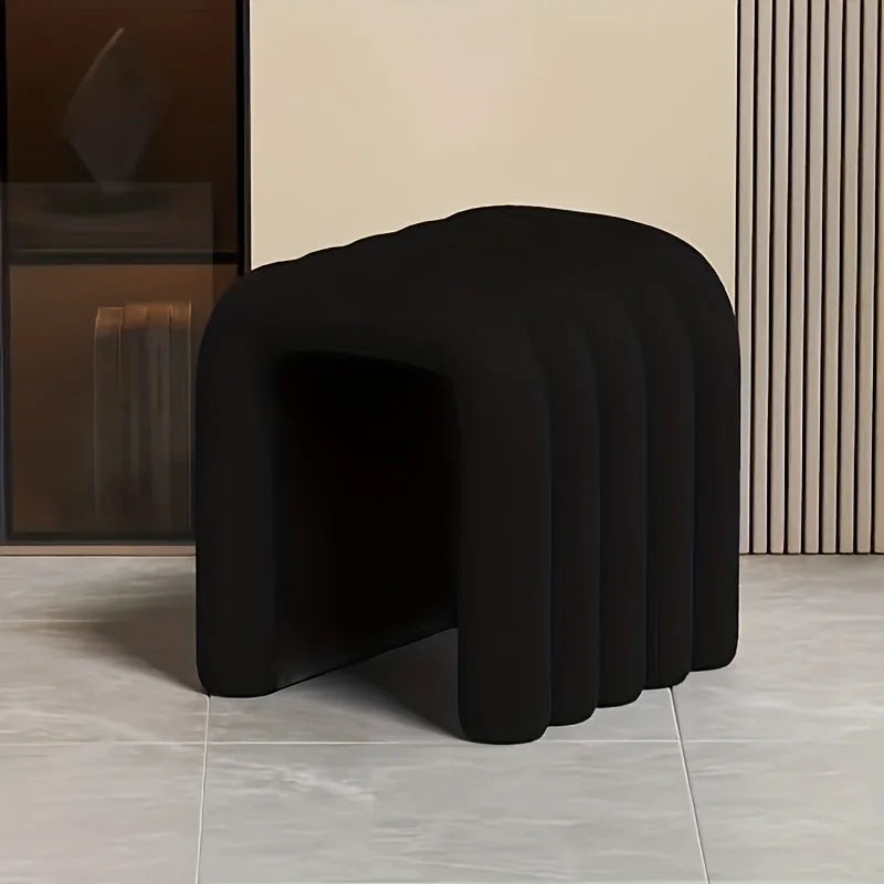 Black, modern stool on a gray floor with a neutral wall background