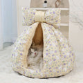 Cat lying in a floral-patterned pet bed with a large bow on top.