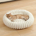 Cat lying on a fluffy white pet bed on a wooden floor