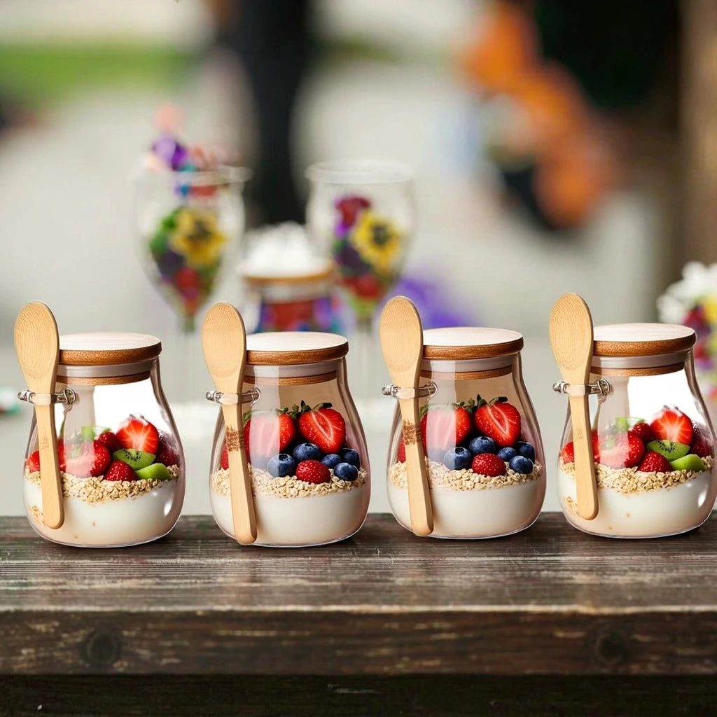 Four glass jars with layered dessert and berries on a wooden surface, with blurred floral decorations in the background.