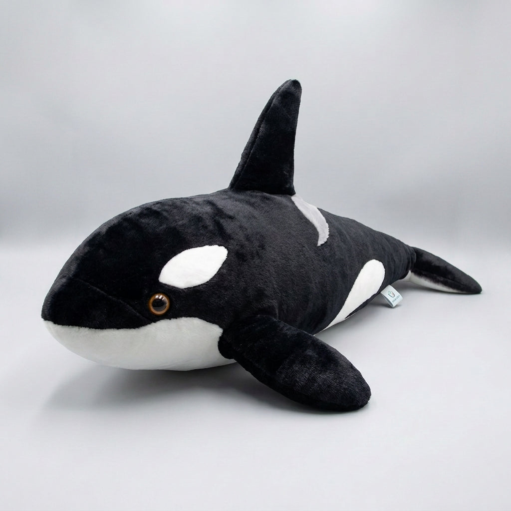 A young girl wearing a pink shorts and a white t-shirt holds a large black and white orca plush toy in a bedroom setting.