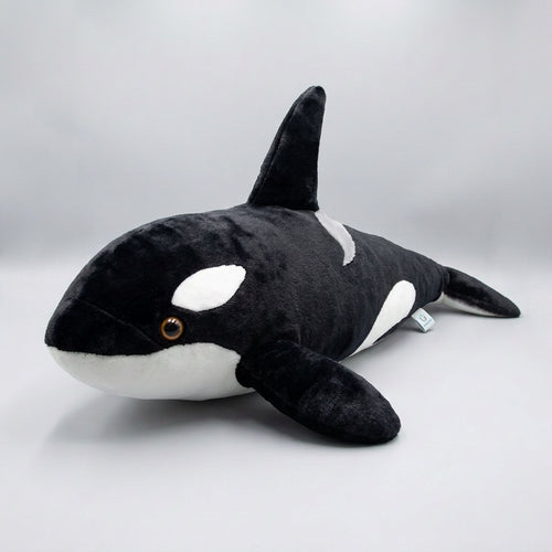 A young girl wearing a pink shorts and a white t-shirt holds a large black and white orca plush toy in a bedroom setting.
