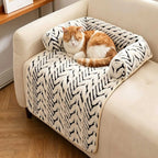 An orange and white cat rests on a plush cream and black patterned pet bed draped over a beige armchair in a bright living room.