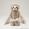 Plush toy sloth on a wooden floor with a bookshelf in the background